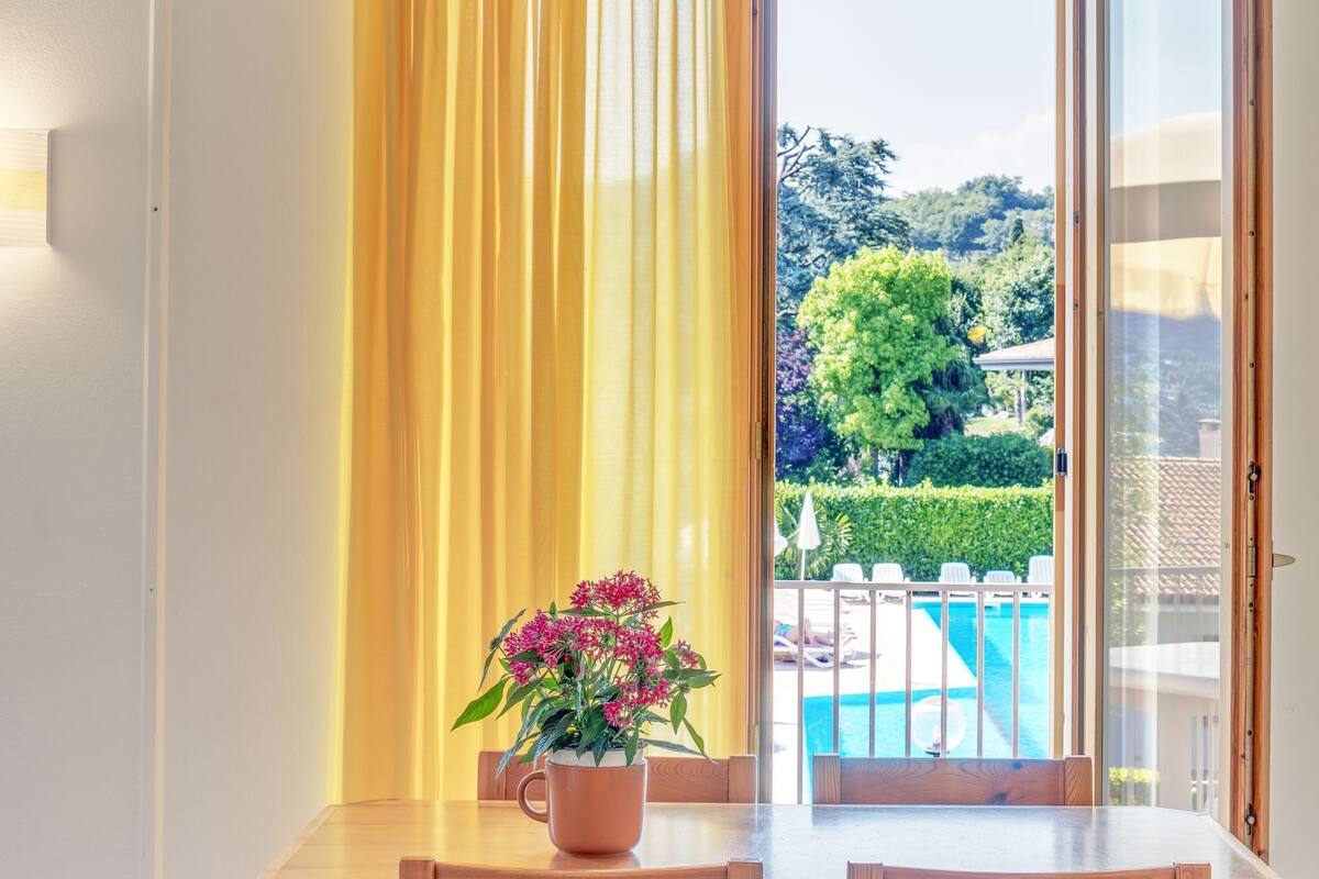 A dining table with chairs, a potted plant, and a view of a swimming pool through an open door.