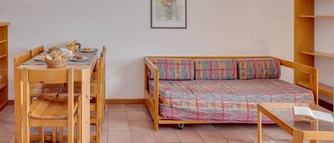 A room with a wooden bed, a dining table with chairs, and a small table with an open book.