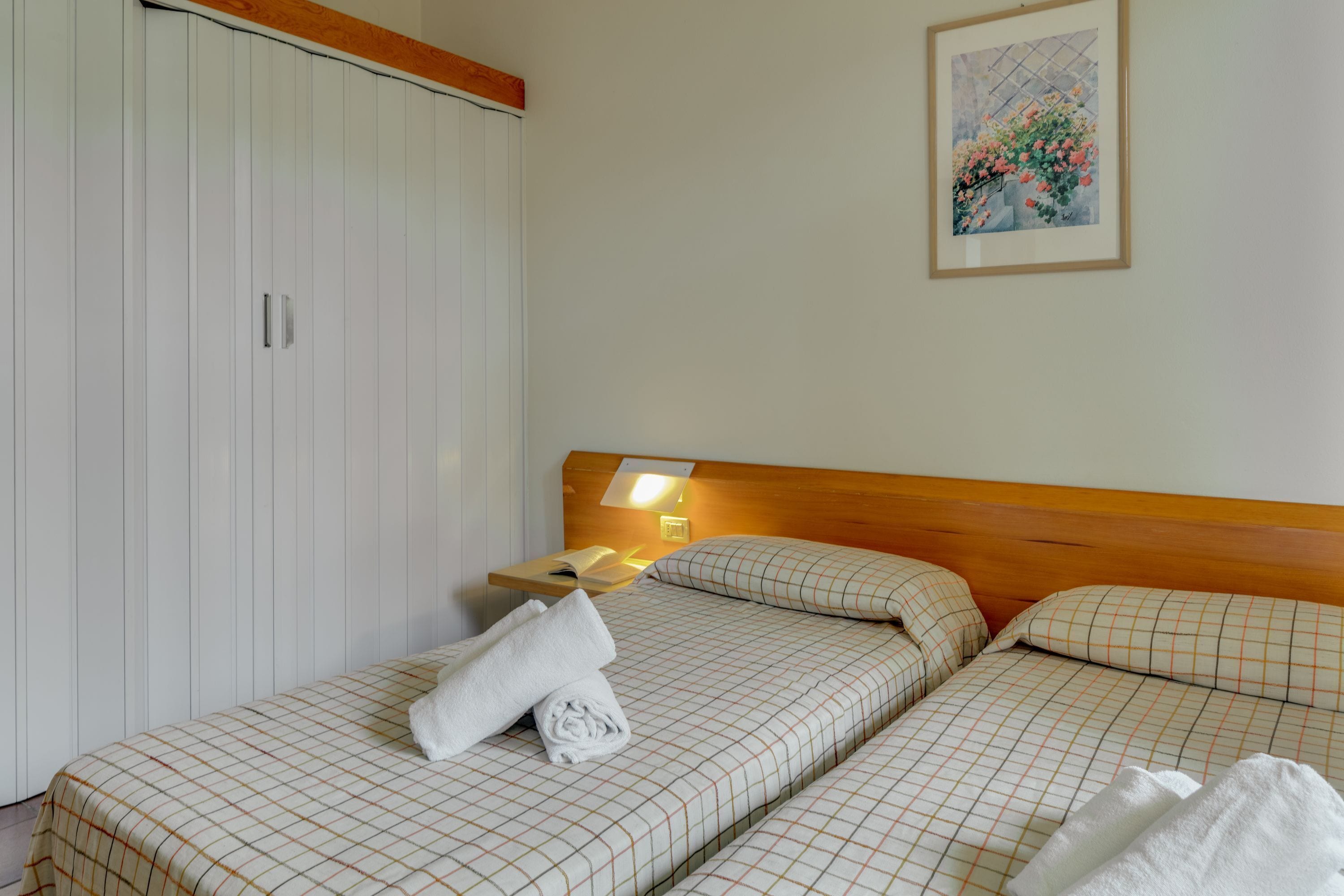 Une chambre d’hôtel avec deux lits, une armoire, une table de chevet avec une lampe et un tableau encadré au mur.