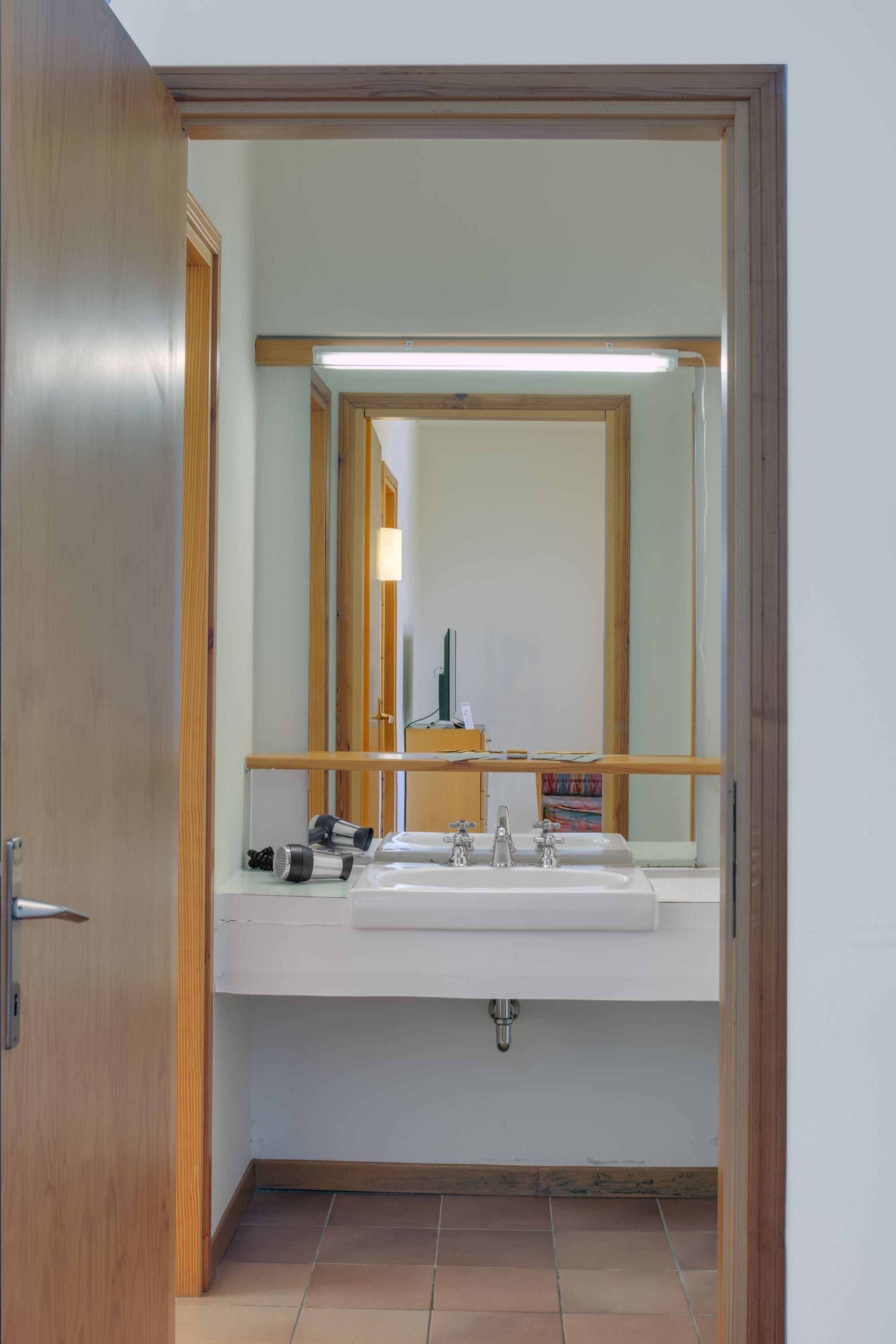 Un baño con puerta de madera, un espejo, un lavamanos y un inodoro.