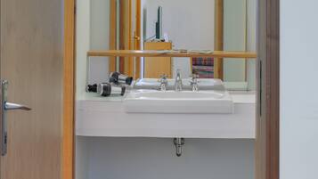 Un baño con puerta de madera, un espejo, un lavamanos y un inodoro.
