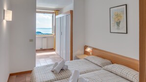 Habitación de hotel con dos camas, una ventana con vistas, un cuadro en la pared y una mesita de noche con lámpara.