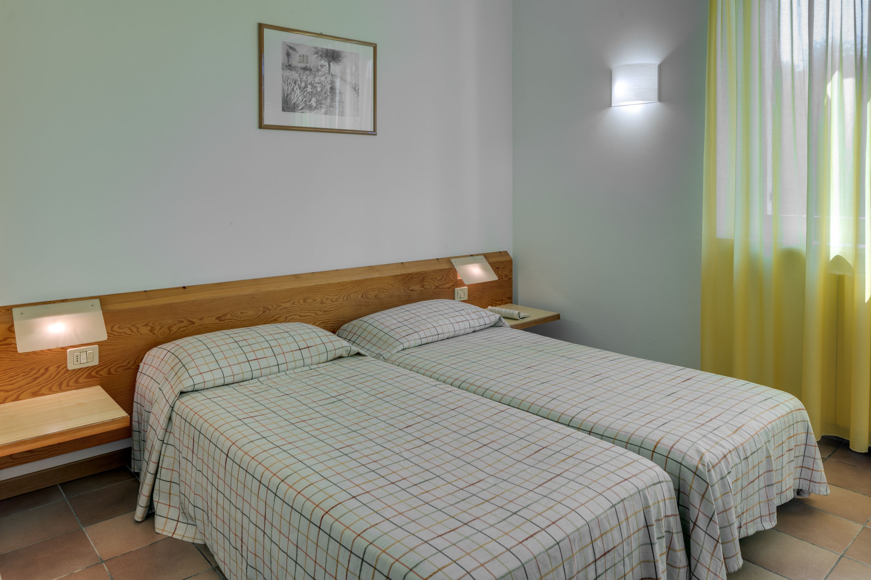 A double bed with a wooden headboard, two bedside tables with lamps, and a framed picture on the wall.