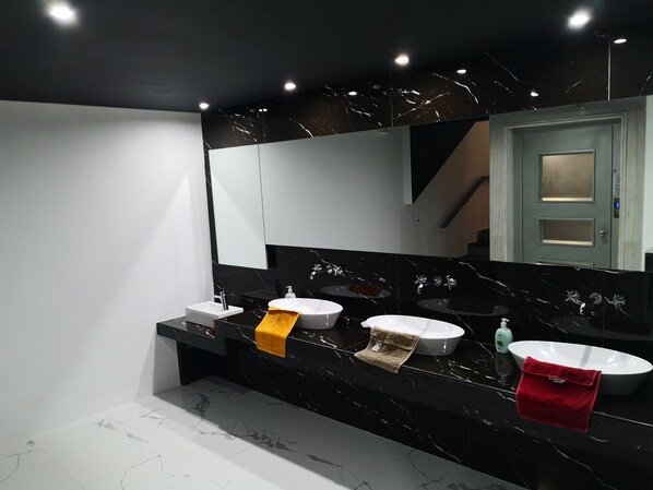 Un baño moderno con tres lavamanos, un espejo grande y una encimera de mármol.