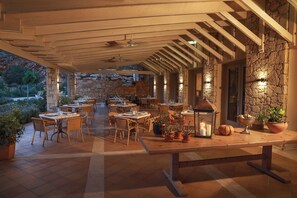Un área de comedor al aire libre con paredes de piedra, vigas de madera y plantas en macetas.