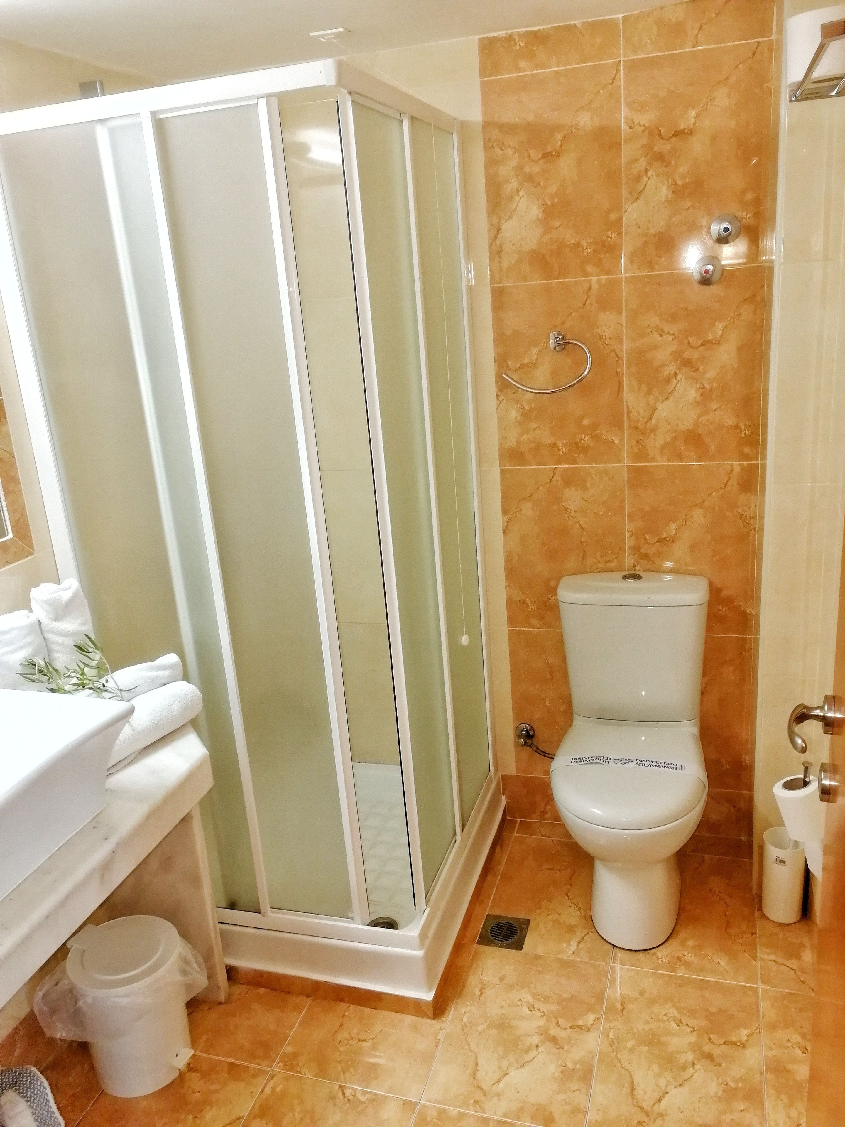 A bathroom with a glass-enclosed shower, a toilet, and a sink with towels.