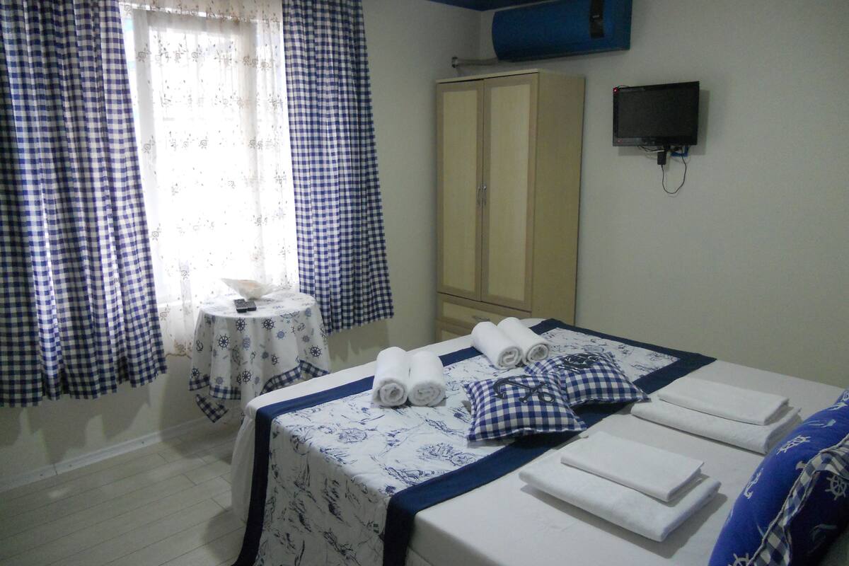 A hotel room with a bed, a wardrobe, a small table with a remote control, and a TV mounted on the wall.