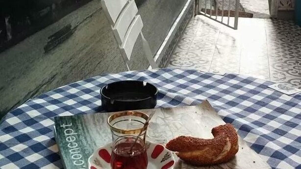 A table with a checkered tablecloth, a book titled 'mundo conceit', a glass of red drink, a baguette, and a small plate with a pastry. - Yacht House Istanbul (Istanbul)