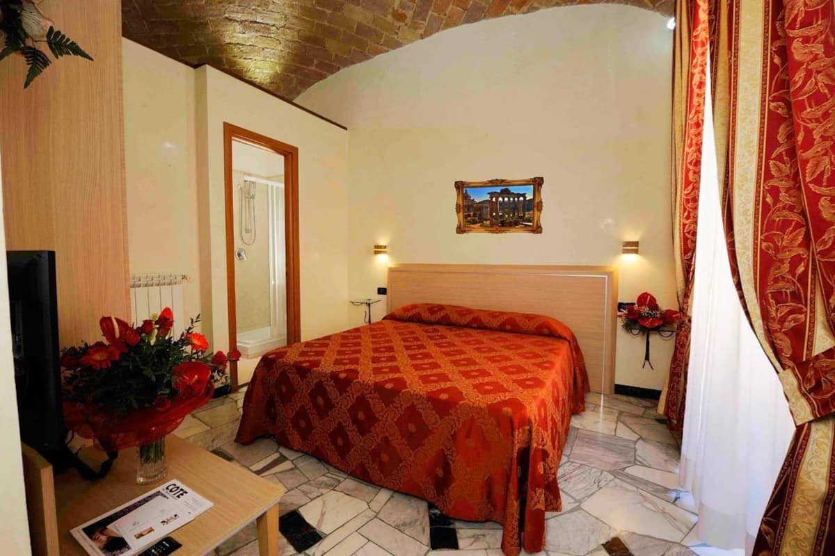 A hotel room with a large bed, a wooden desk with a vase of flowers, a framed picture on the wall, and a door.