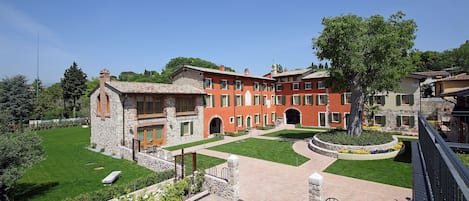 A courtyard with a stone building, a tree, and a paved walkway.