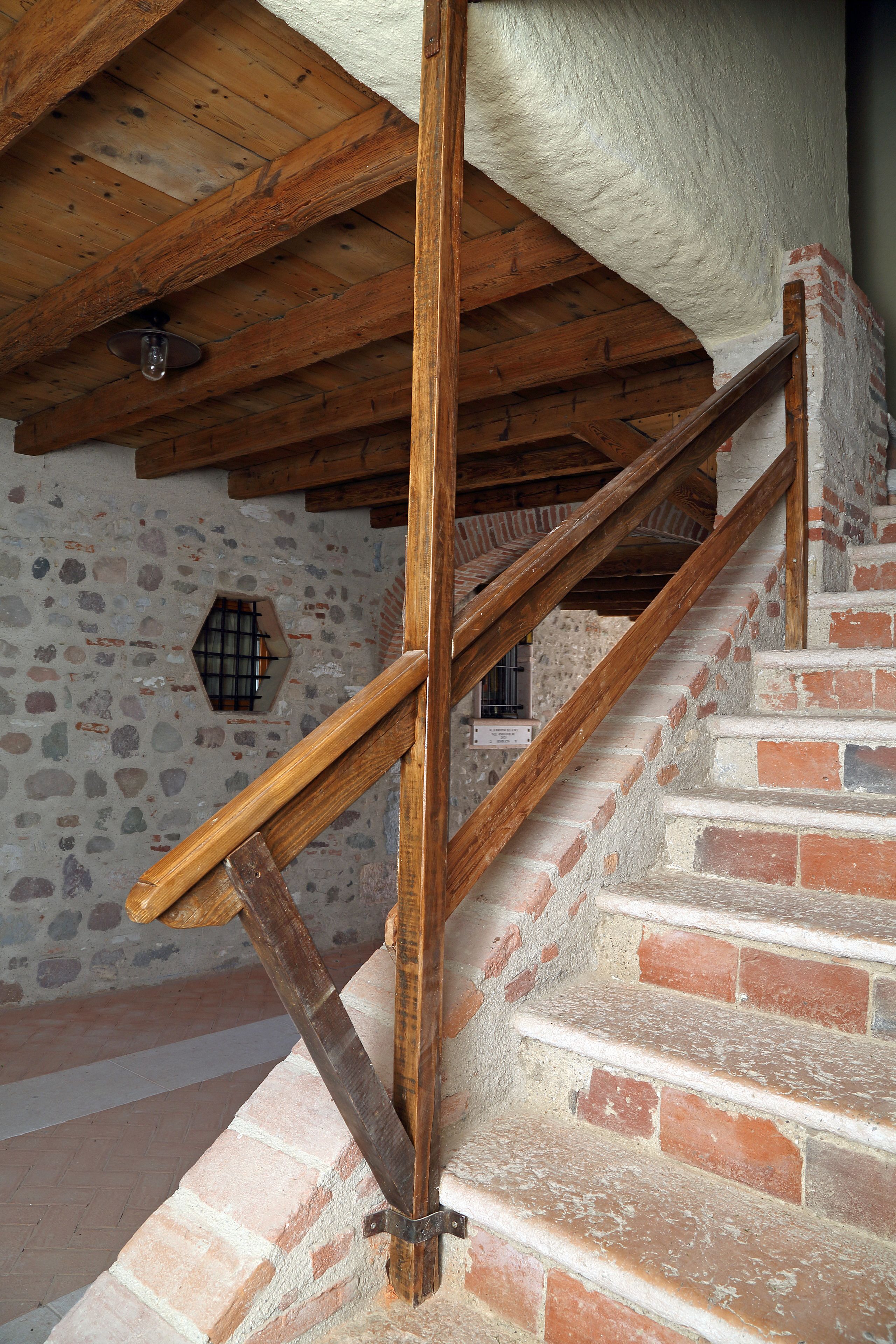 A wooden staircase with a brick wall and a stone floor.