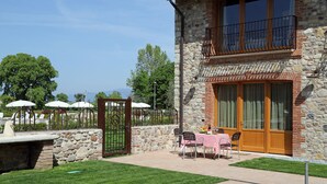 A stone building with a balcony, a patio with chairs and a table, and a stone wall. - Residence Borgo Mondragon (Lazise)