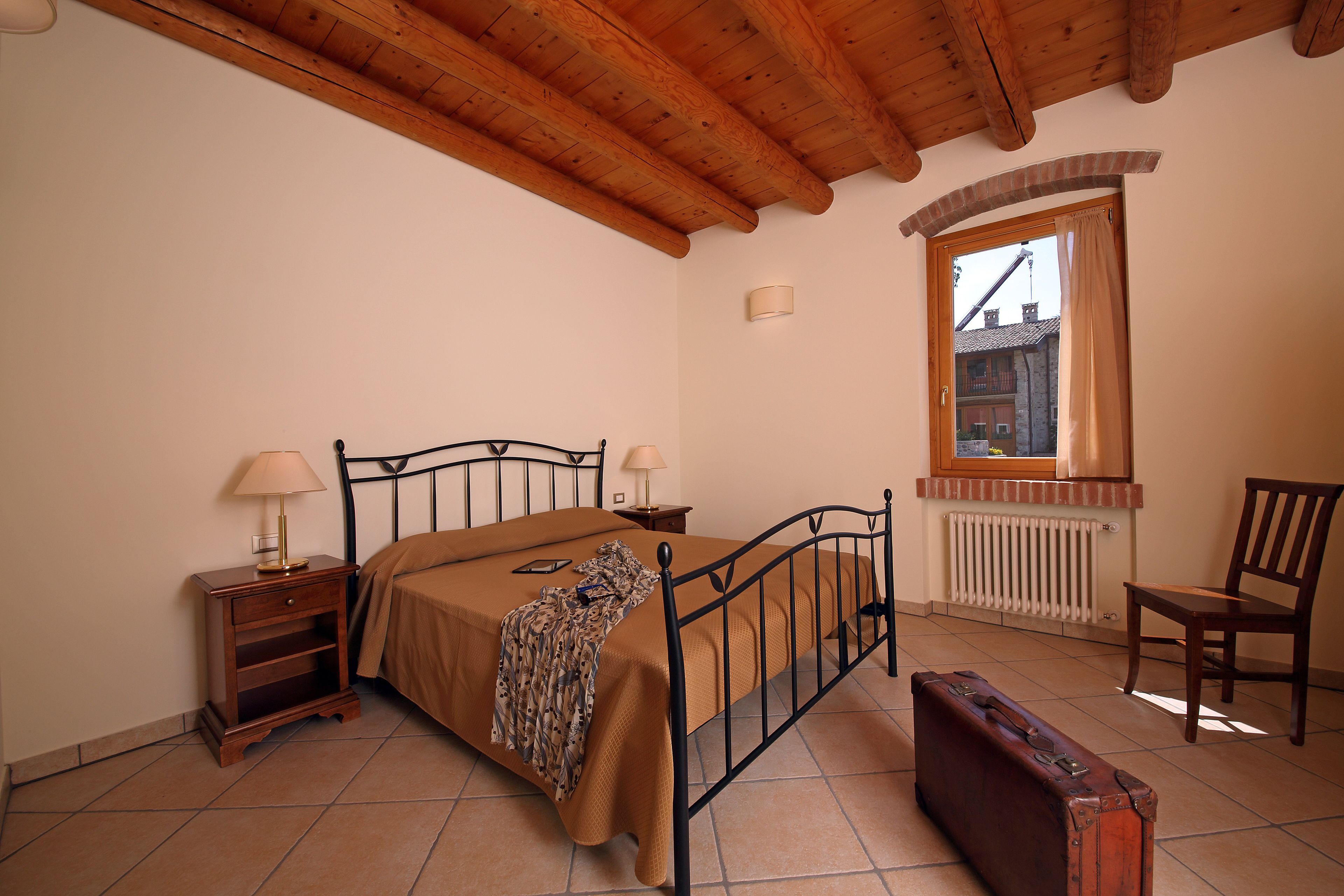 A bedroom with a bed, bedside tables, a chair, a window, and a radiator.