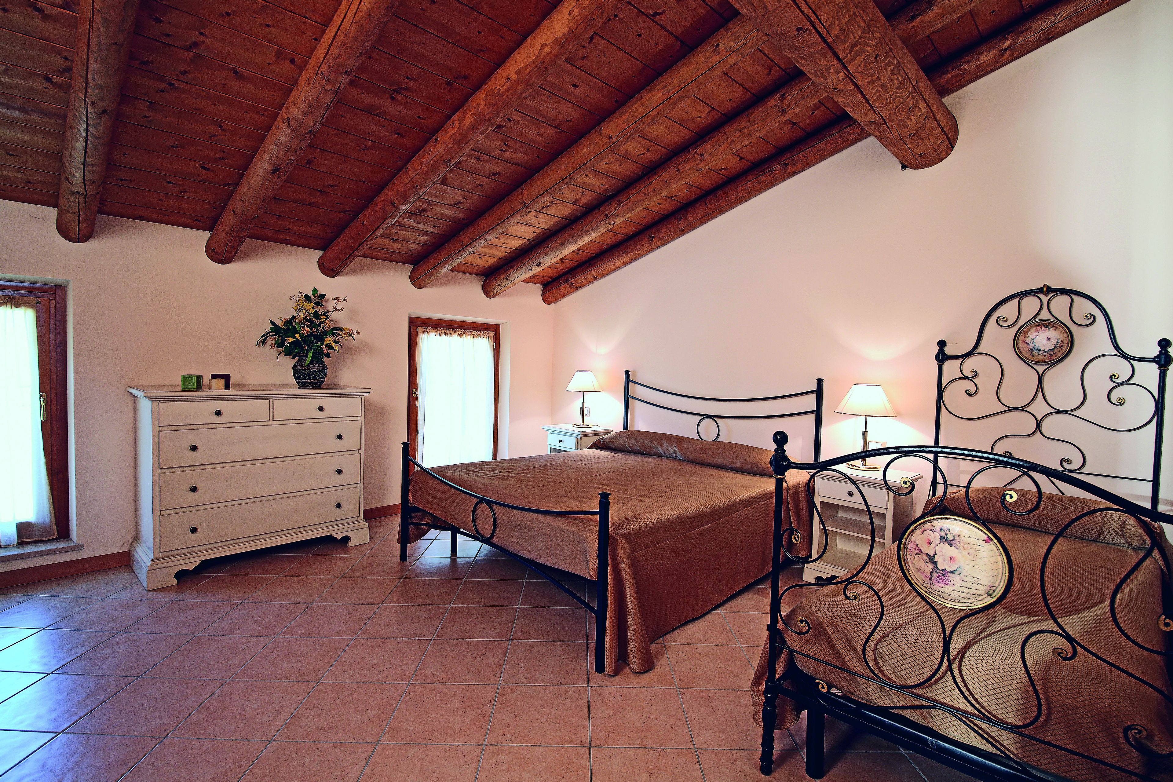 Une chambre avec un plafond en bois, un lit avec un cadre en métal, une commode et une table de chevet avec des lampes.