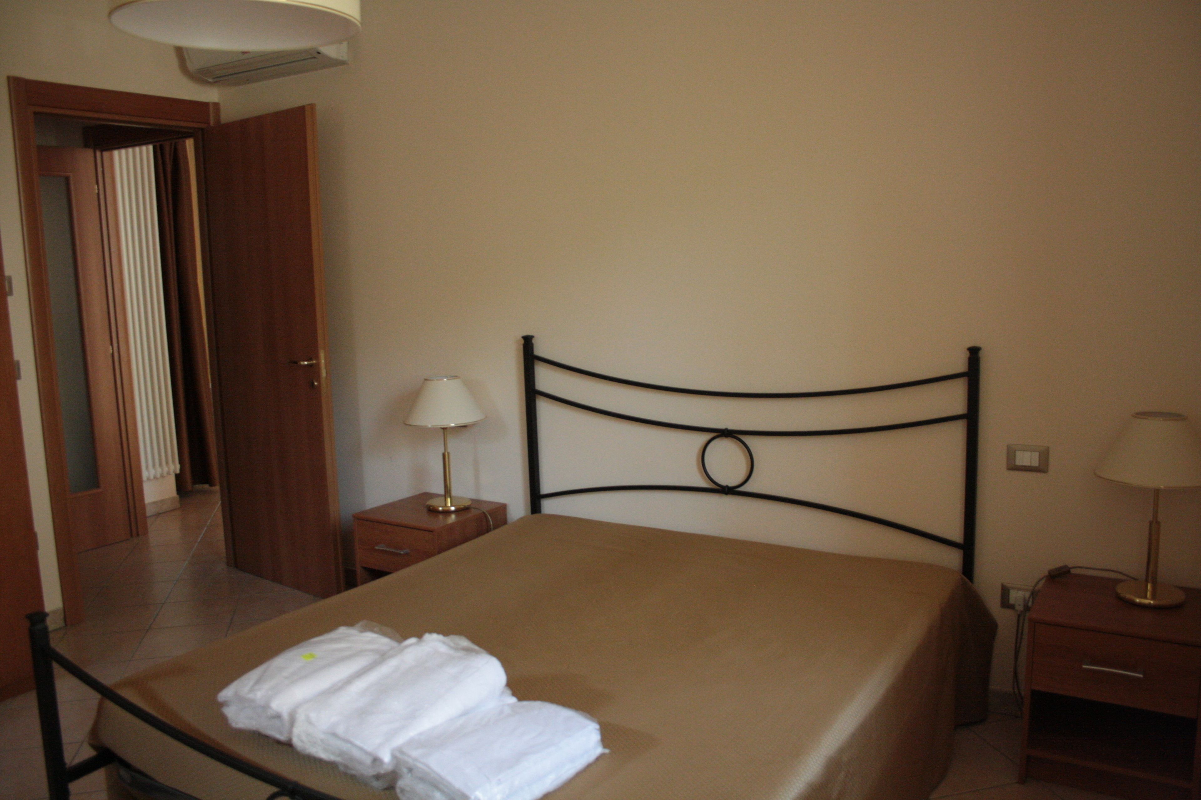A hotel room with a bed, two bedside tables, a lamp on each table, and a door leading to another room.