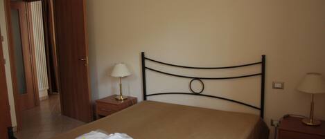 A hotel room with a bed, two bedside tables, a lamp on each table, and a door leading to another room.