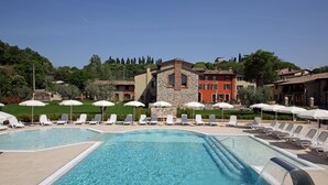 A swimming pool with lounge chairs and umbrellas, surrounded by buildings and greenery. - Residence Borgo Mondragon (Lazise)
