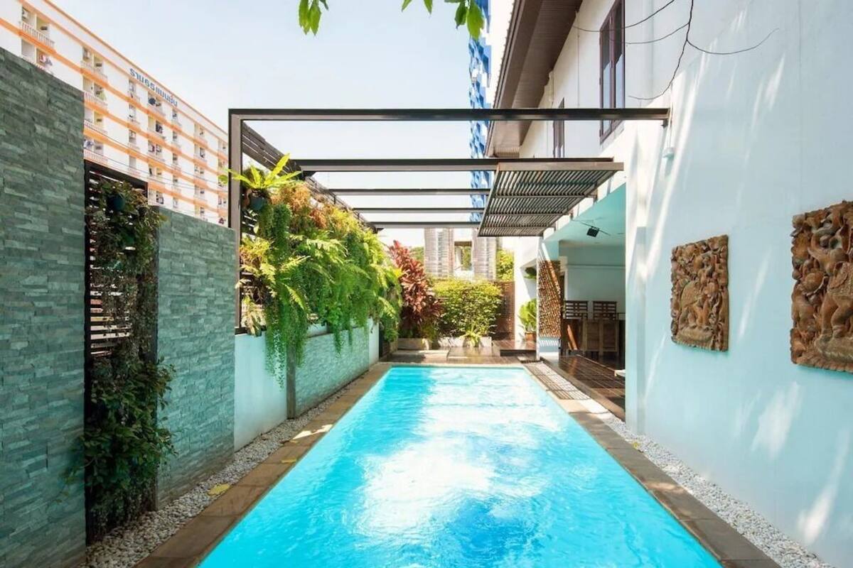 A swimming pool with a clear blue water surface, surrounded by a stone wall and a wooden deck.