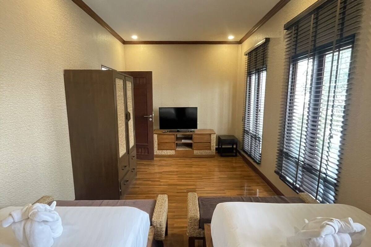 A hotel room with two beds, a TV, a desk, and a window with blinds.