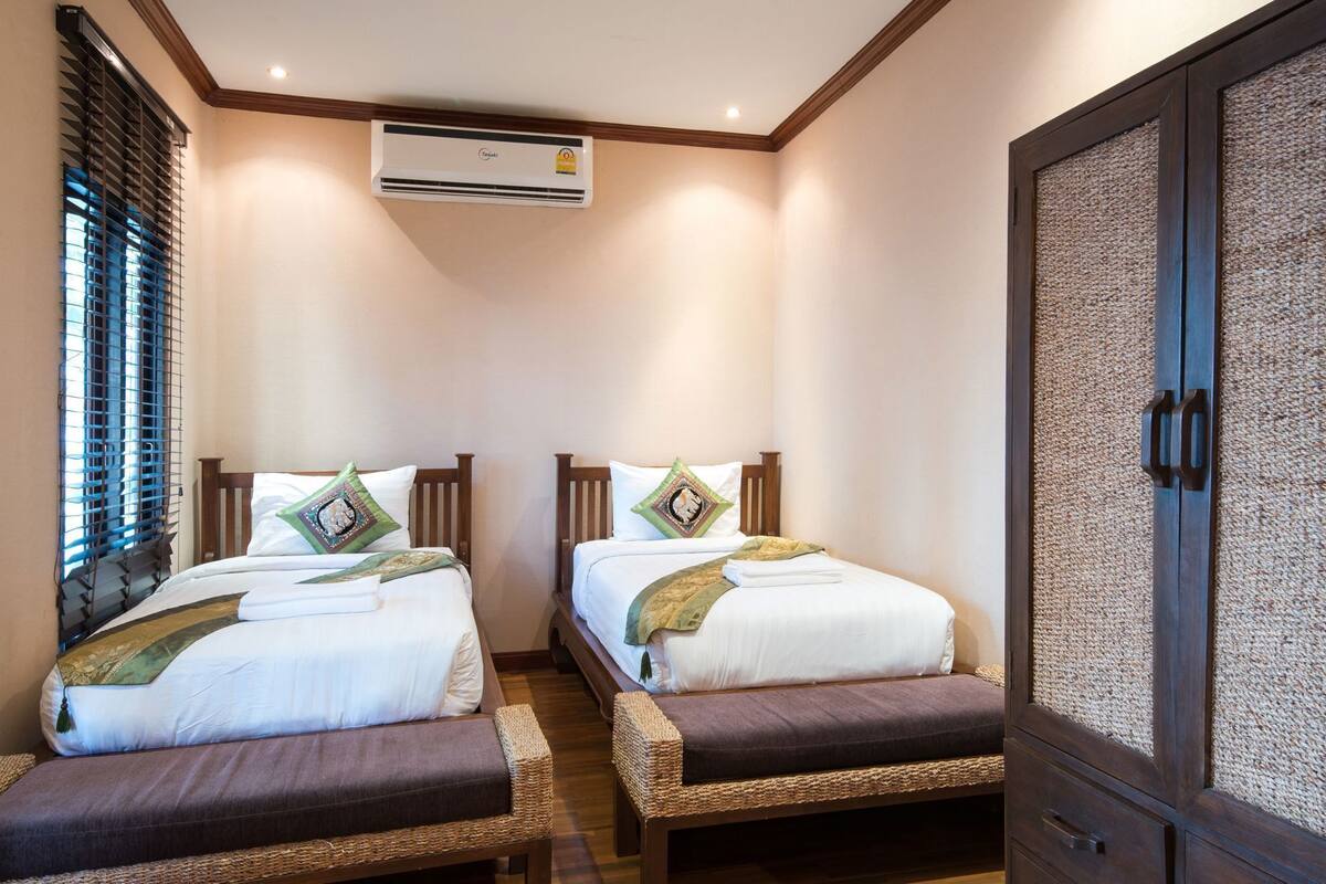 A hotel room with two beds, a wardrobe, and an air conditioning unit.