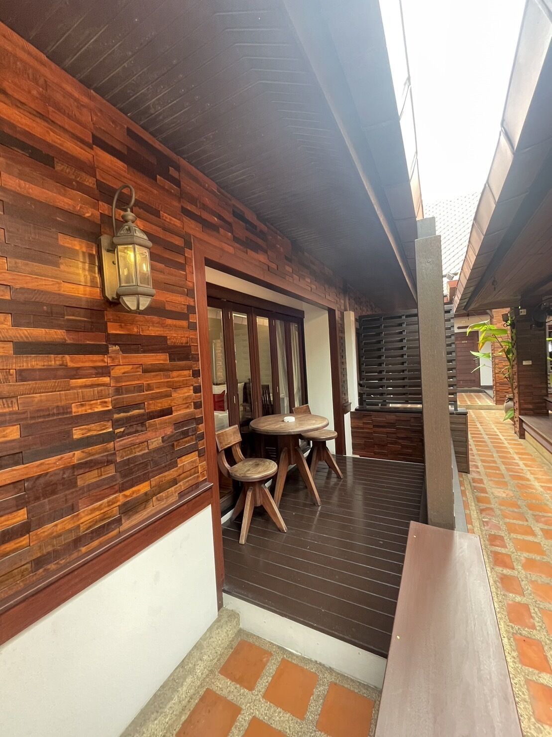 An outdoor patio area with wooden flooring, a brick wall, and a wooden bench.