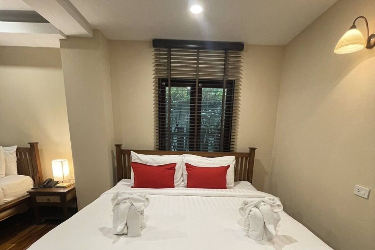 A neatly made bed with white and red pillows, a wooden headboard, and a bedside lamp.