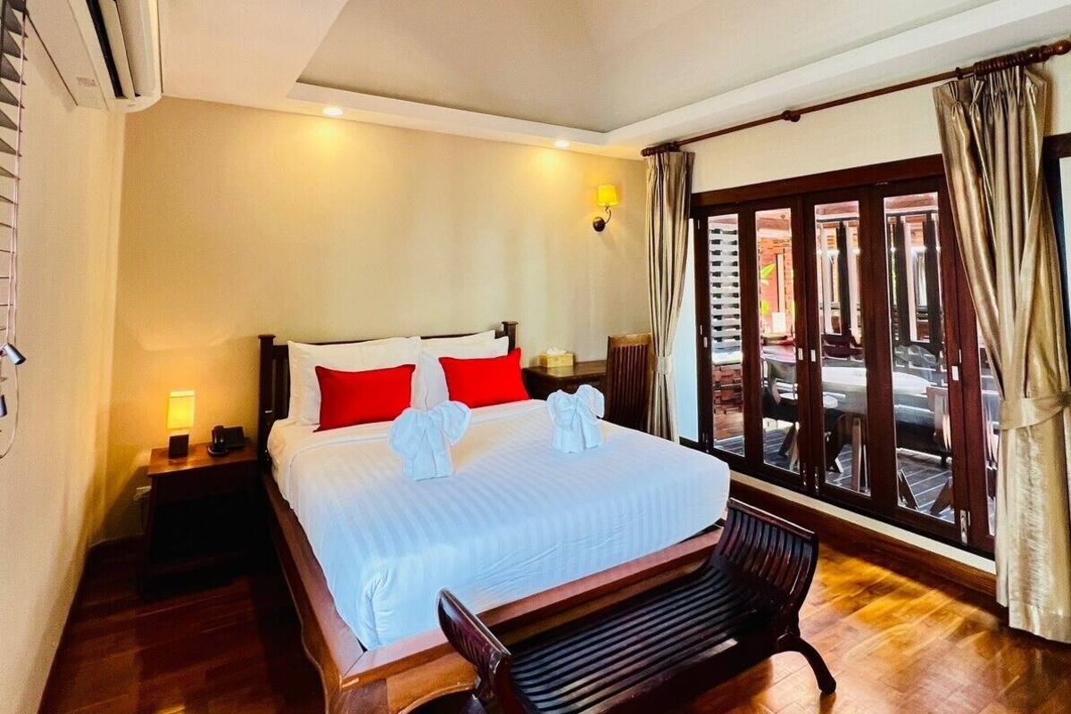 A hotel room with a large bed, wooden flooring, a bench, a nightstand, and a window with curtains.