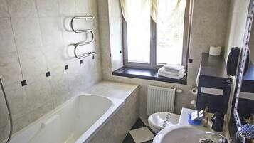 A bathroom with a bathtub, toilet, sink, and a window with curtains.