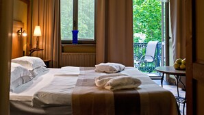 Habitación de hotel con dos camas, una ventana con persianas, una mesa con fruta y un balcón con una silla.