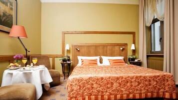 Quarto de hotel com uma cama grande, uma mesinha com café da manhã, uma cadeira e uma janela com cortinas.