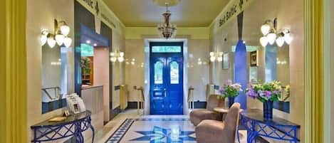 A hotel lobby with a star-patterned floor, a reception desk, seating area, and a blue door.