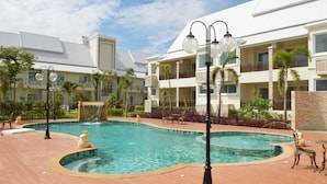 A swimming pool with a waterfall feature, surrounded by a patio area with outdoor furniture and lamp posts. - Nantrungjai Boutique Hotel (Nan)