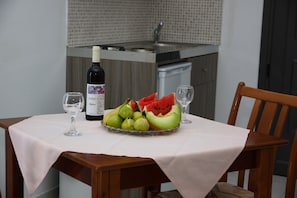 A dining table with a bottle of wine, a bowl of fruit, and two wine glasses. - Villa Marina (Hersonissos)