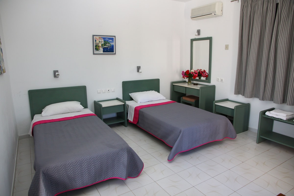 A hotel room with two single beds, a small desk, a mirror, and a window with curtains.