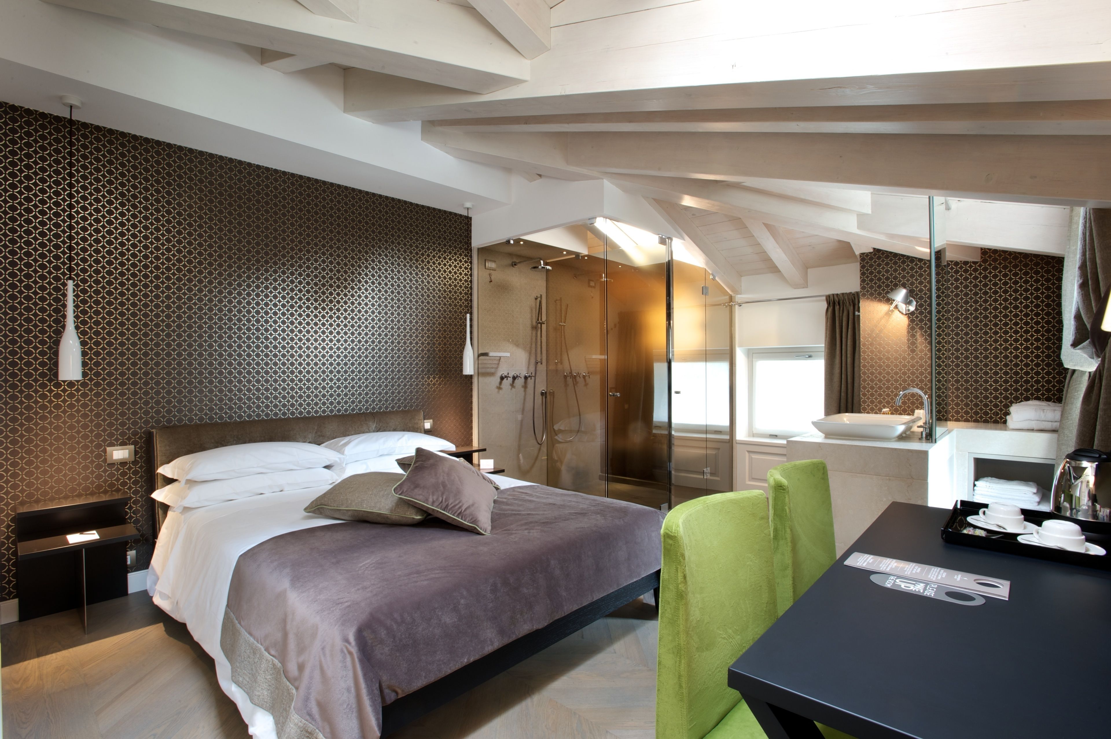 Een moderne hotelkamer met een groot bed, een bureau, een groene stoel, een badkamer met een glazen douche en een wastafel.
