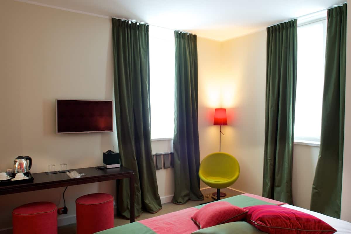 A hotel room with a bed, a desk, a chair, a TV, and a lamp.