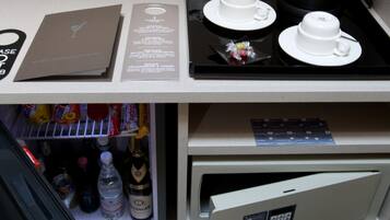 A minibar with a coffee maker, cups, and a laptop.