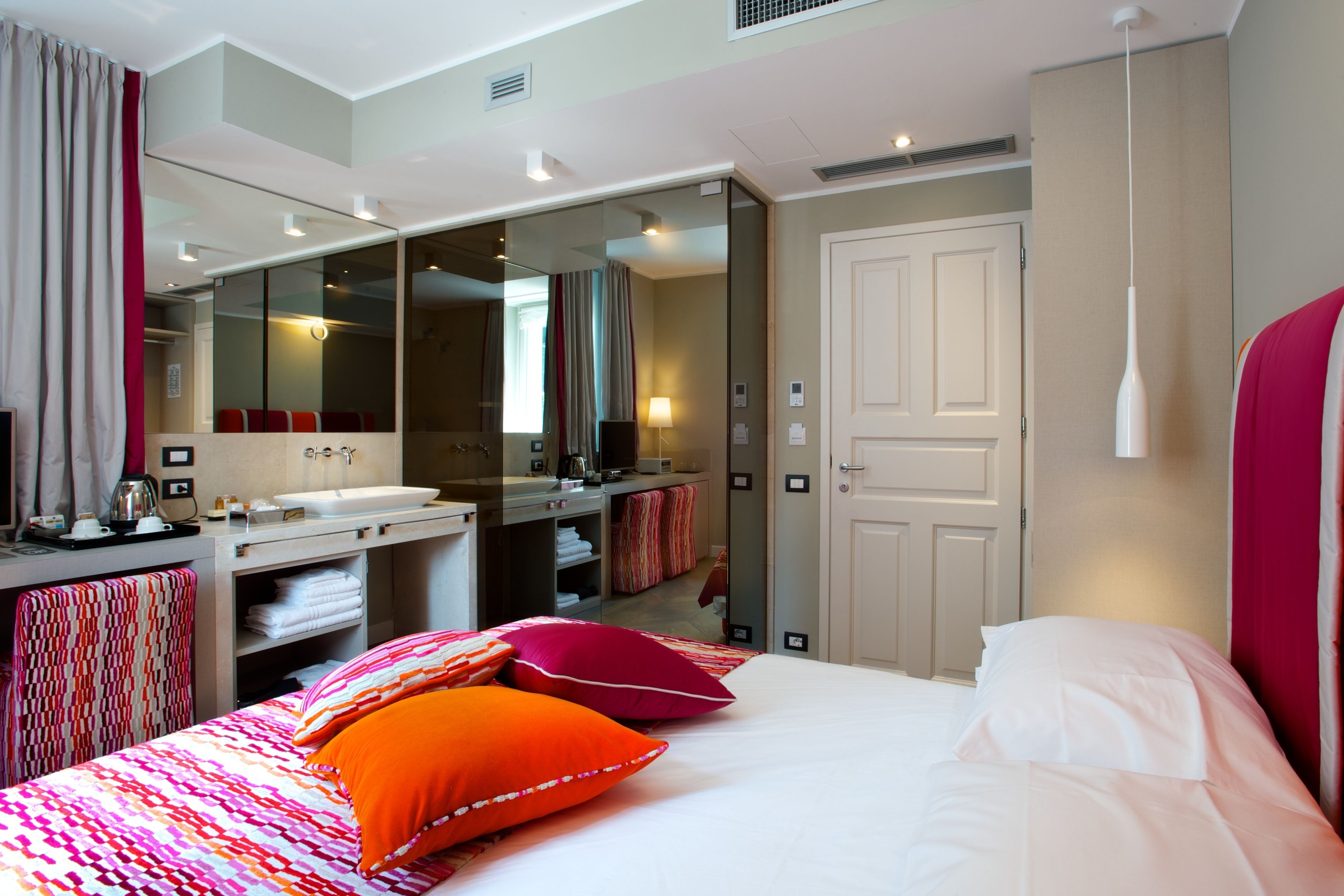 A modern hotel room with a large bed, a bathroom with a mirror, and a desk with a sink.