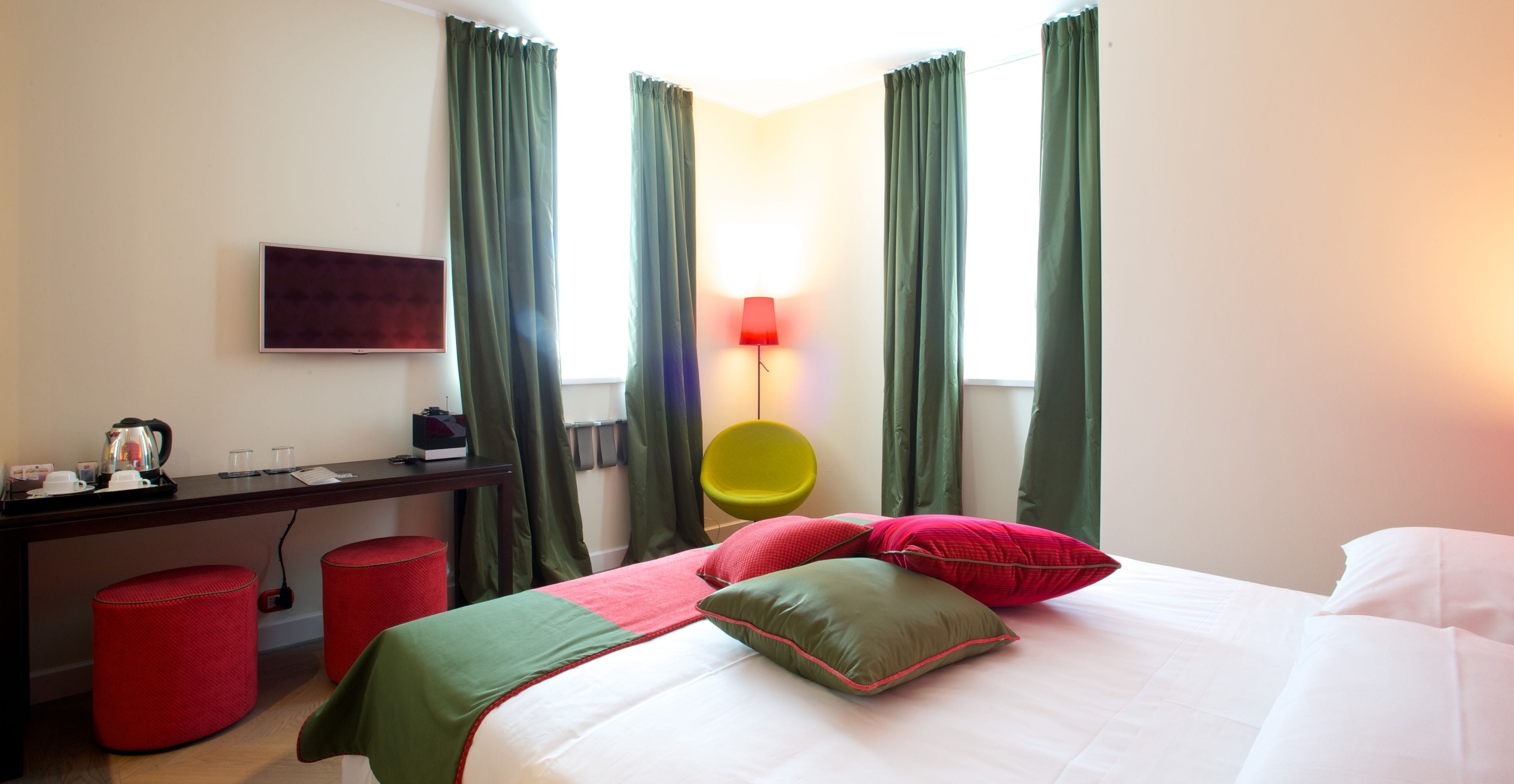 Una habitación de hotel con cama, escritorio, silla, televisor y cortinas.