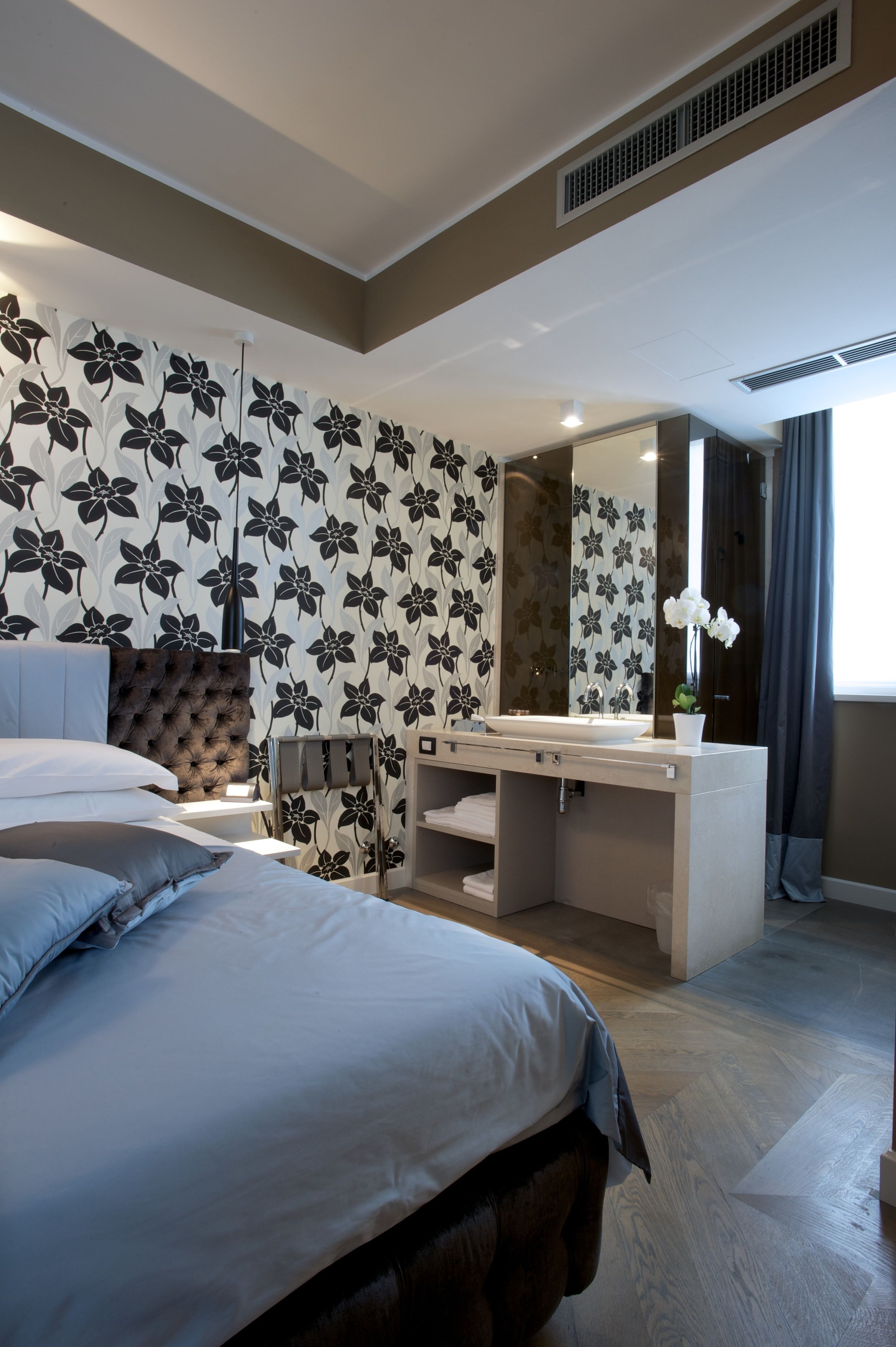 A modern bedroom with a large bed, a vanity with a mirror, and a floral-patterned wall.