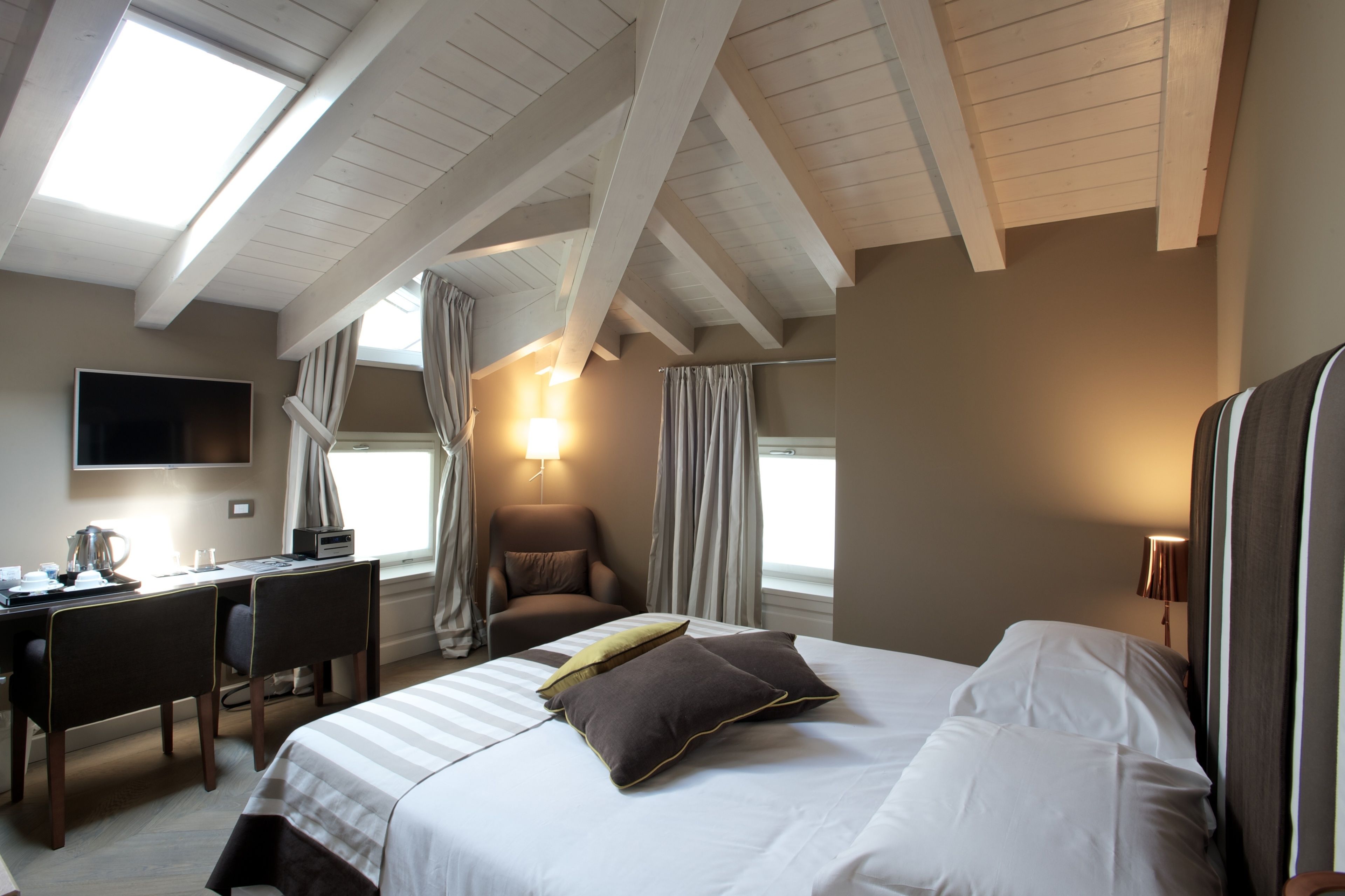 A hotel room with a bed, desk, and chair, a TV on the wall, and a window with curtains.