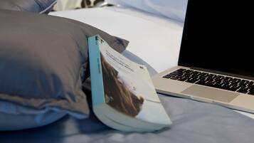 A bed with a laptop, pillows, and a book on a bed with a floral wallpaper background.