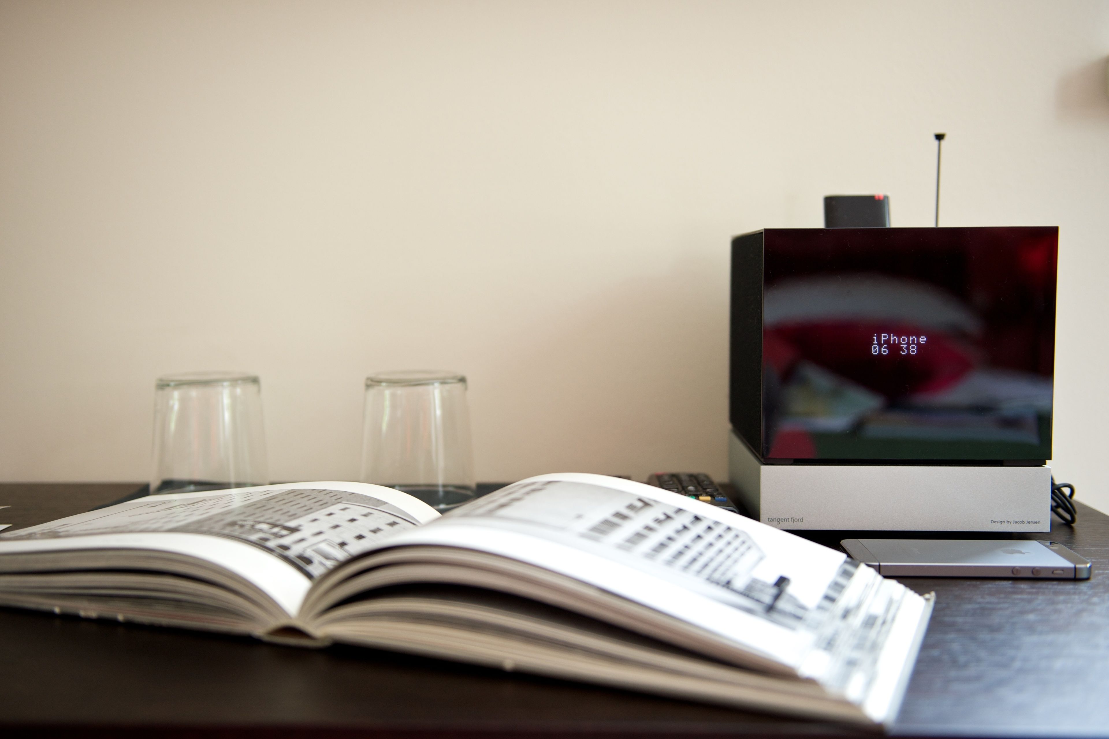 A desk with an open book, a smartphone, and a television displaying an iPhone interface.