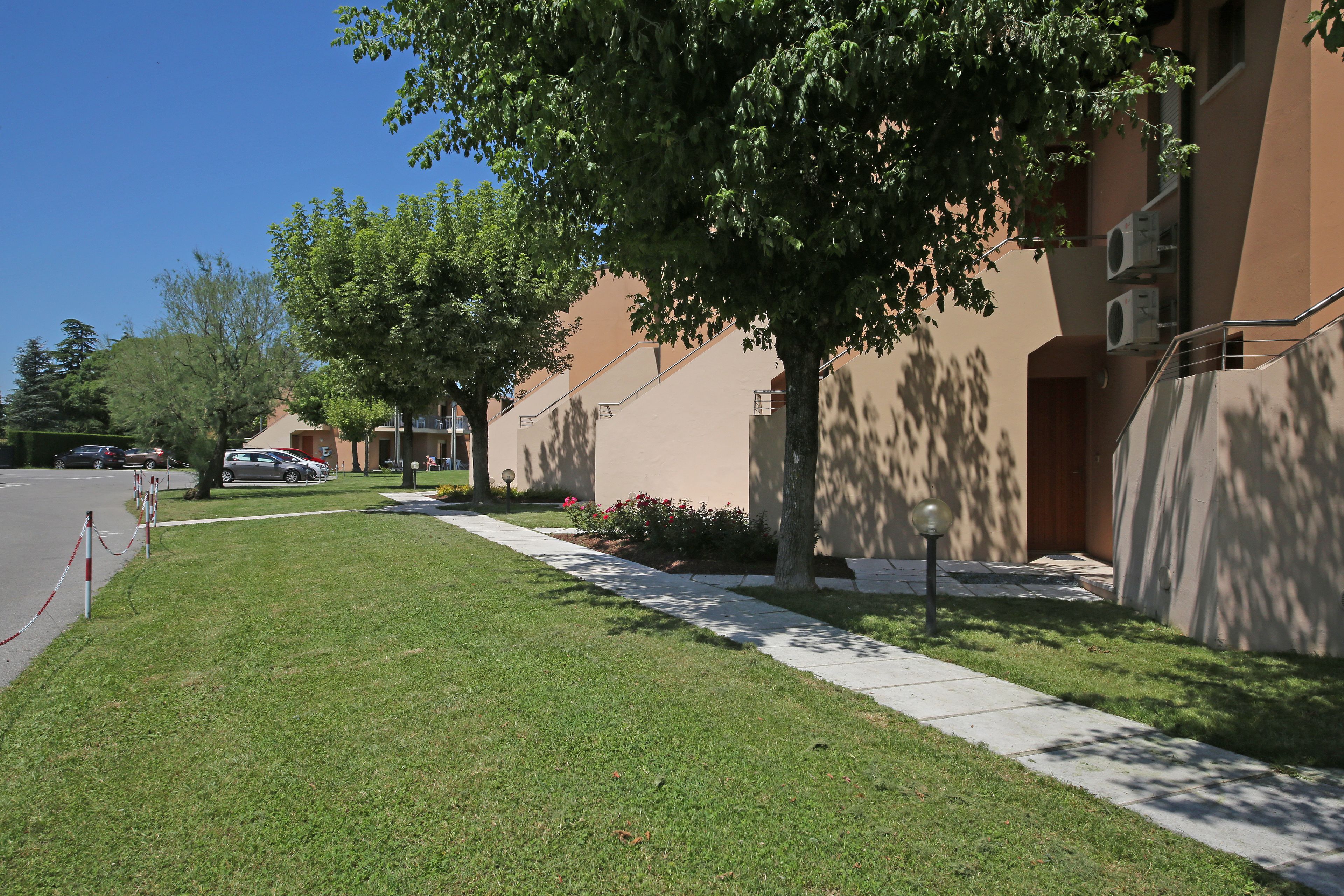 A residential area with a well-maintained lawn, a sidewalk, and a row of apartment buildings.