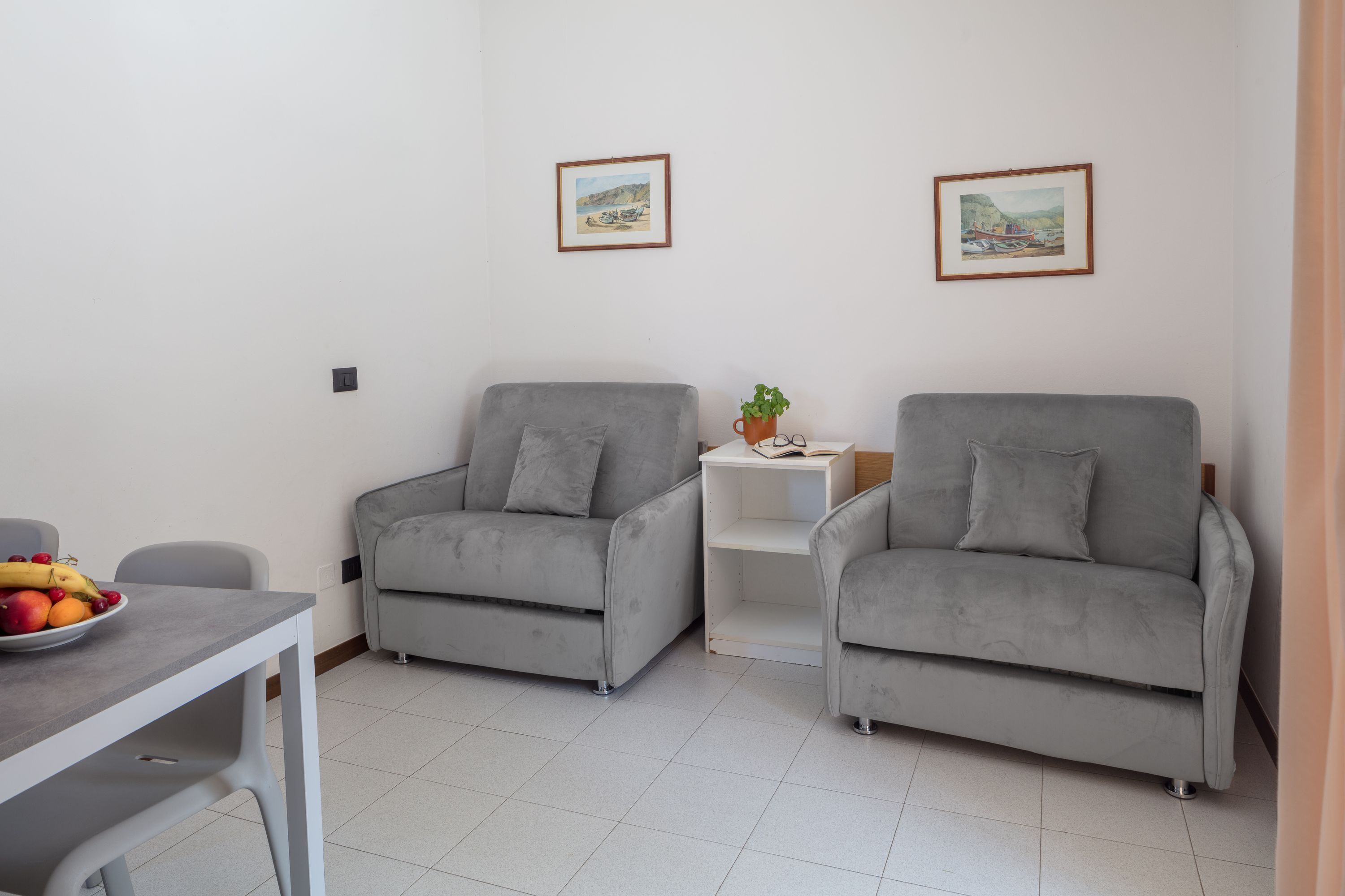 Un salon moderne avec deux canapés gris, une petite table sur laquelle on a posé des fruits, et deux tableaux encadrés accrochés au mur.