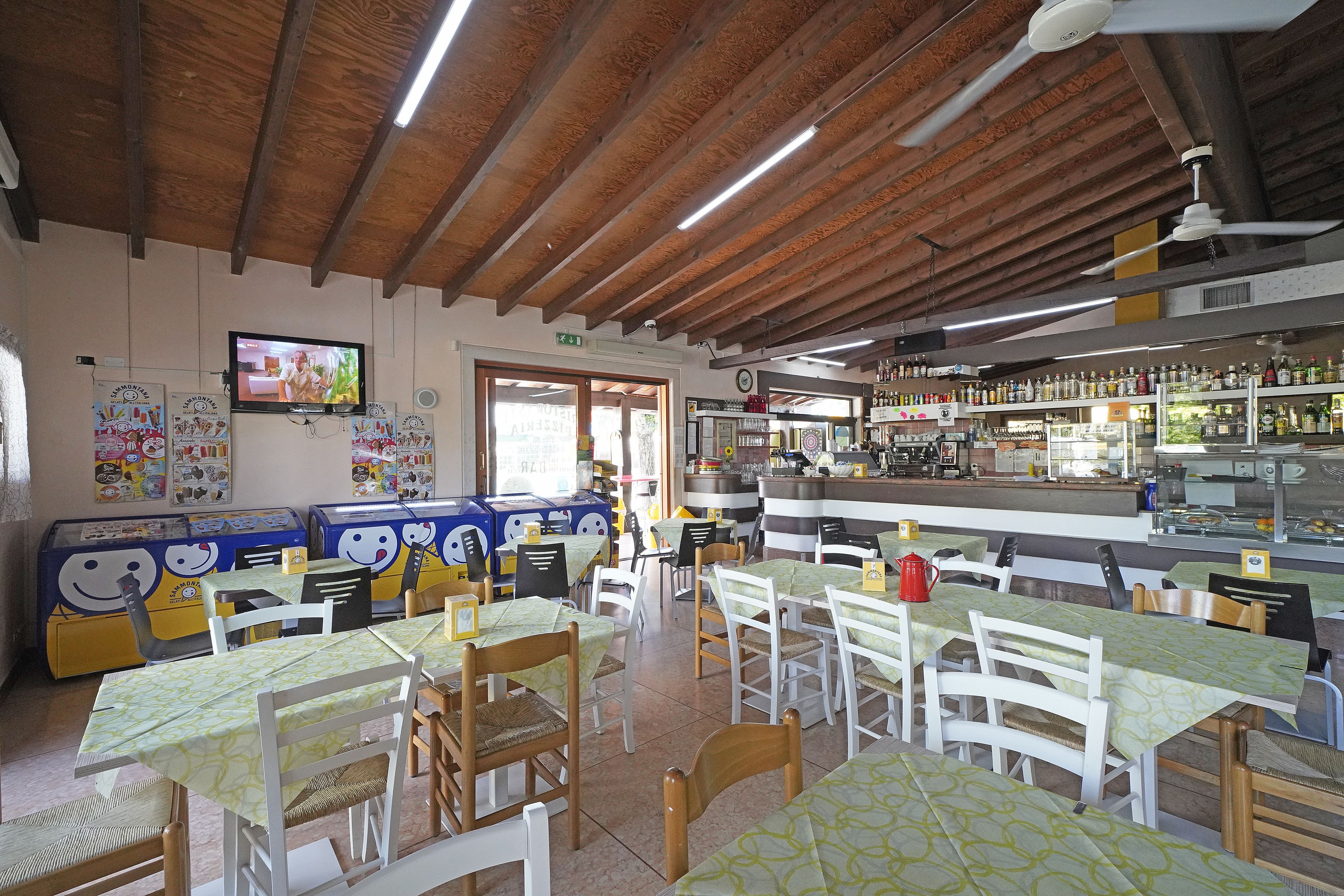 Un restaurant avec des poutres en bois au plafond, des tables recouvertes de nappes vertes et un bar où sont exposées différentes bouteilles.