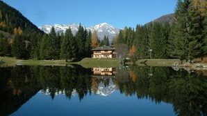 A lodge with a reflection in a lake, surrounded by trees and mountains. - Appartamenti Pellizzano (Pellizzano)