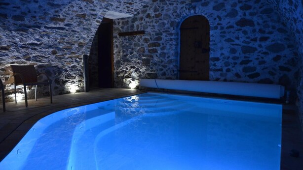 A stone-walled room with a pool, a wooden door, and a chair. - Appartamenti Pellizzano (Pellizzano)