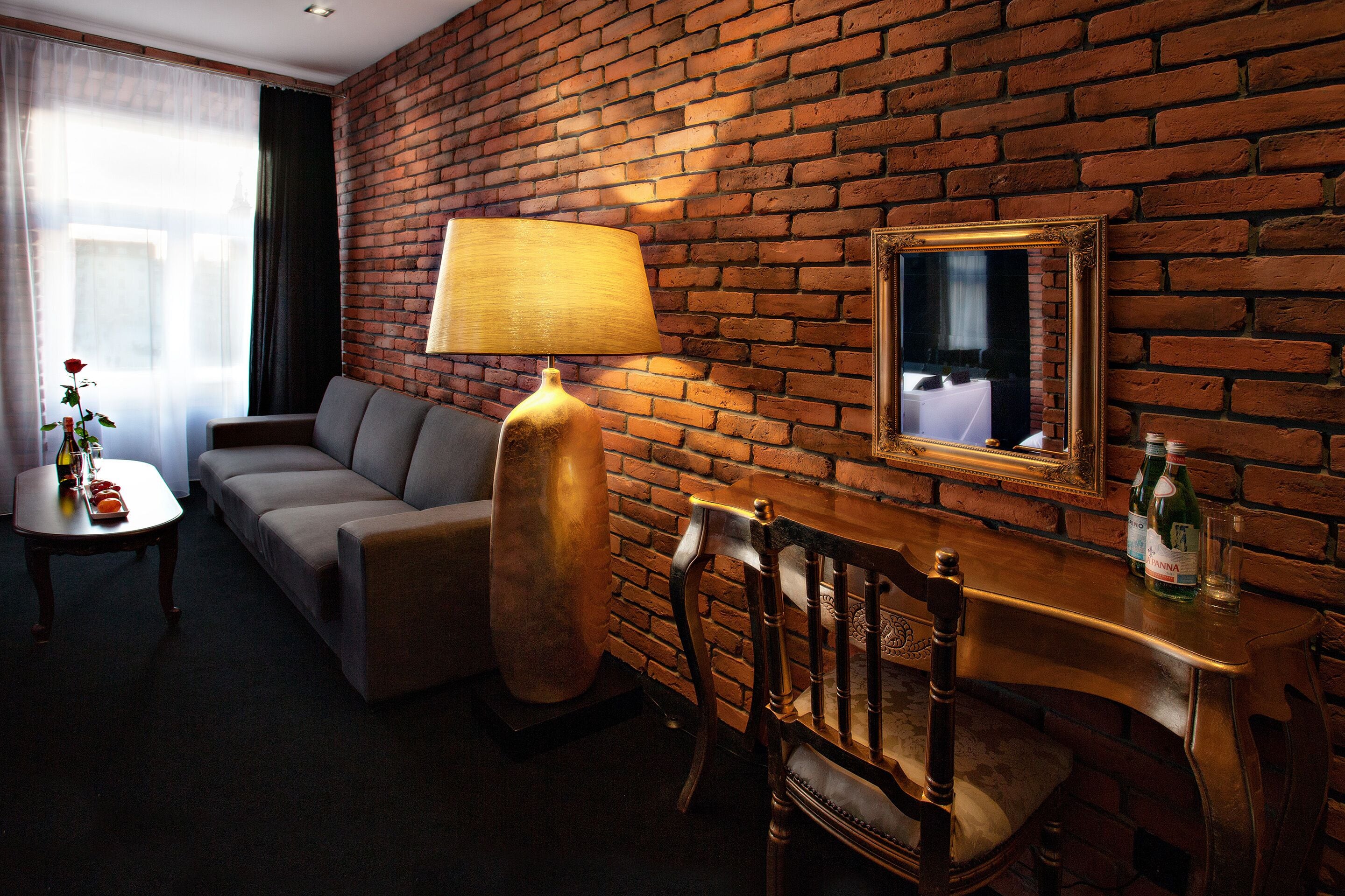 A room with a brick wall, a sofa, a table with a lamp, a chair, and a mirror.