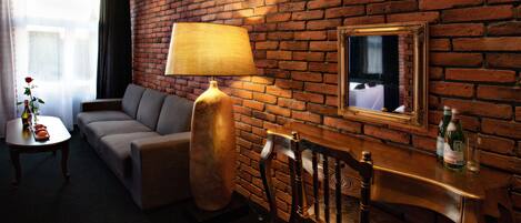 A room with a brick wall, a sofa, a table with a lamp, a chair, and a mirror.